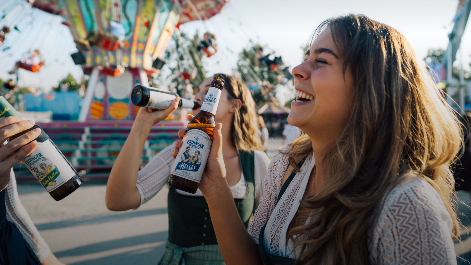 A woman is laughing and holding an ERDINGER Brauhaus Helles in her hand at a folk festival.