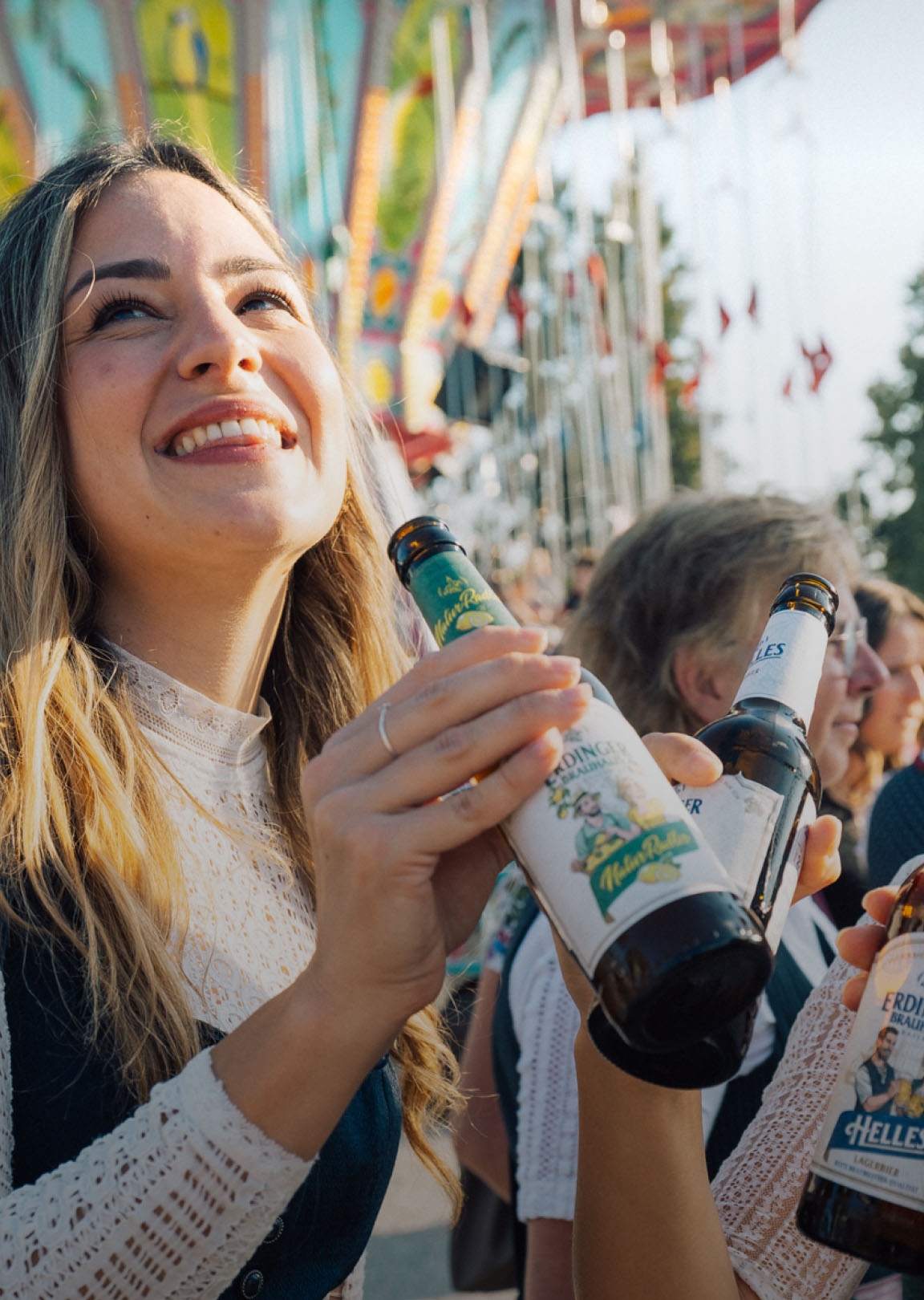 A woman is laughing and holding an ERDINGER Brauhaus Helles in her hand at a folk festival.