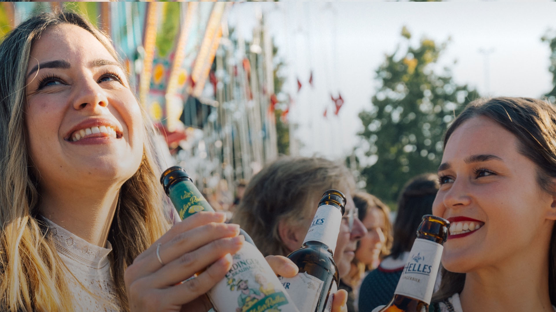 A woman is laughing and holding an ERDINGER Brauhaus Helles in her hand at a folk festival.