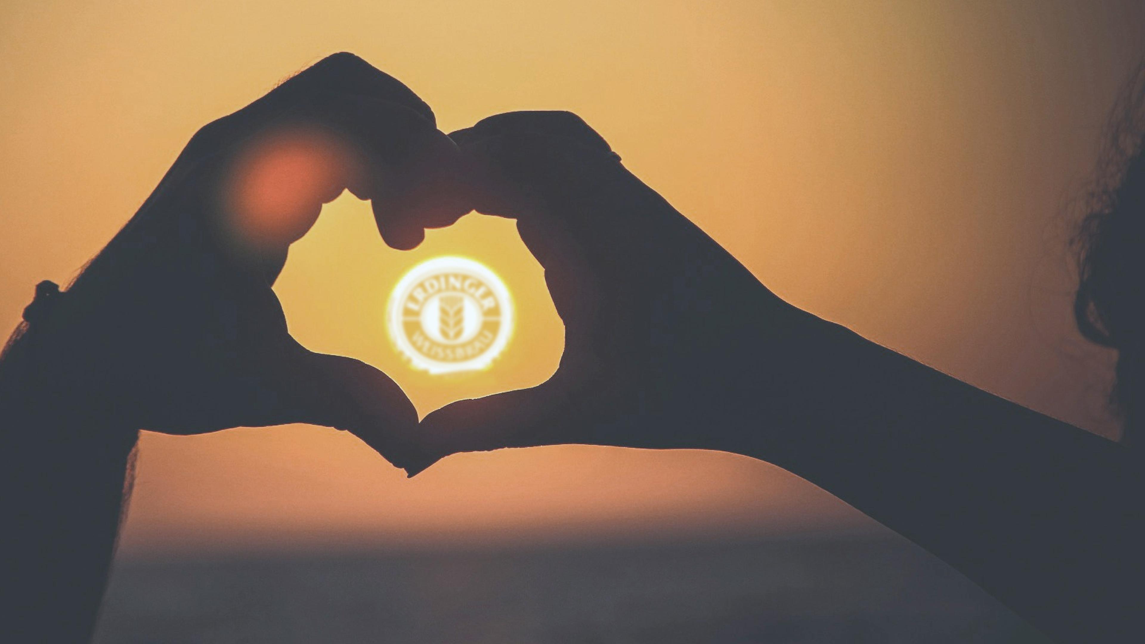 Hands form a heart around the setting sun with the ERDINGER logo, representing Fischer‘s donation check as a sustainability project.