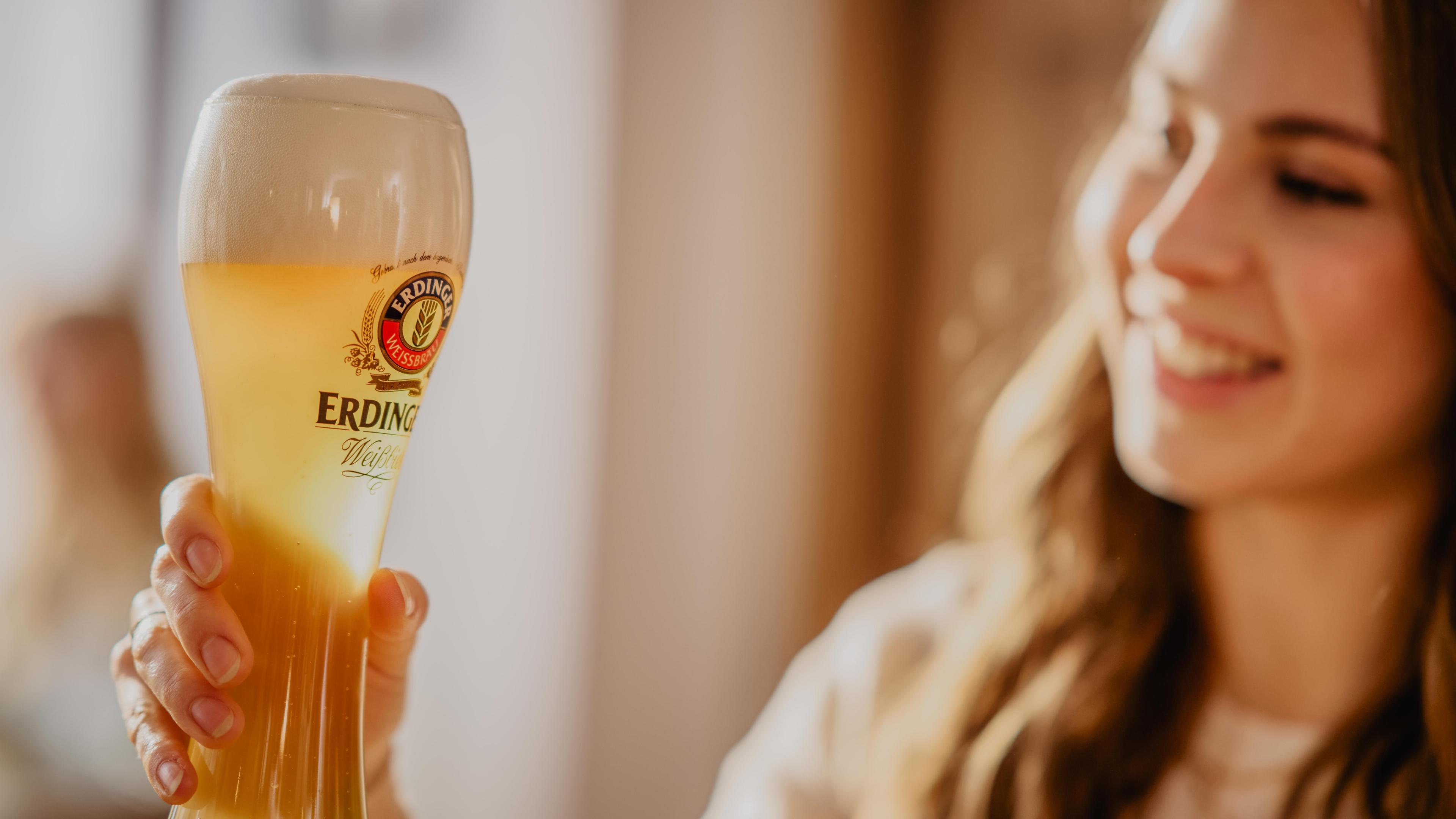 A woman holds a glass of ERDINGER wheat beer up to the light.