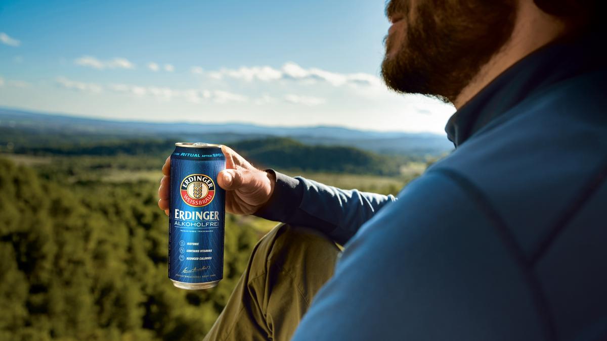 A man sits on a summit, gazing into the distance with an ERDINGER Alkoholfrei in hand.