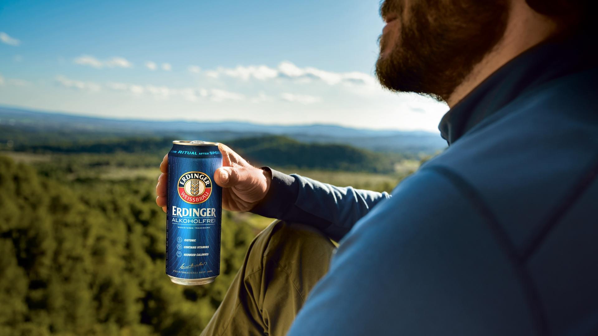 A man sits on a summit, gazing into the distance with an ERDINGER Alkoholfrei in hand.