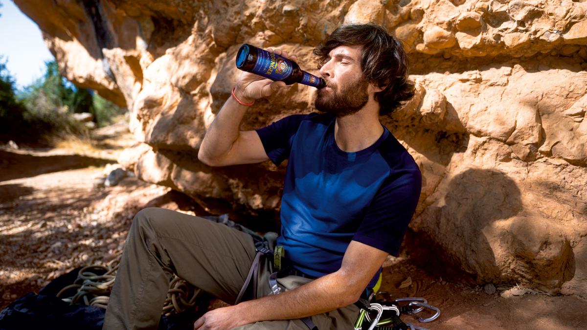 A man sits on a summit, gazing into the distance with an ERDINGER Alkoholfrei in hand.