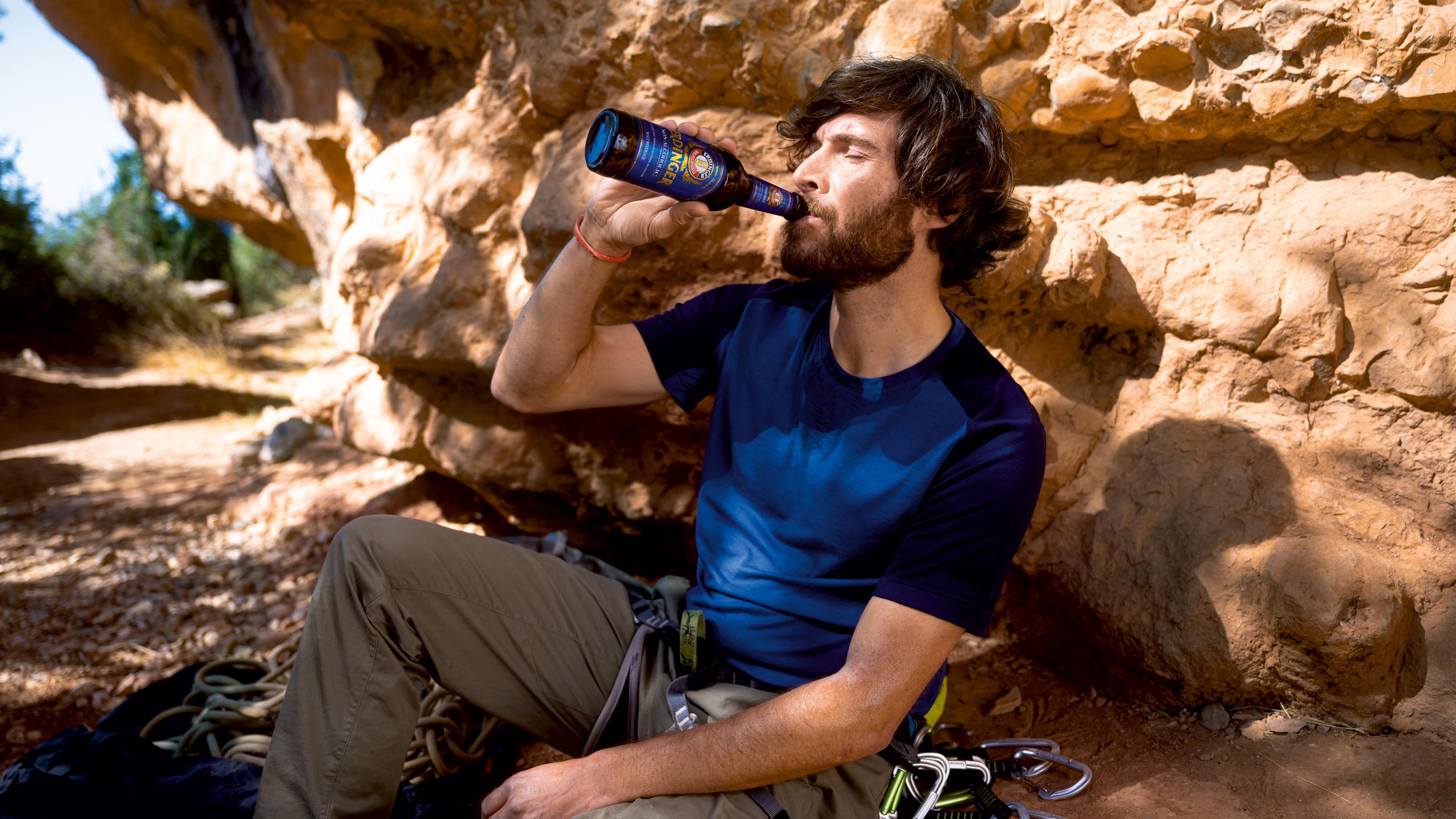 A man sits on a summit, gazing into the distance with an ERDINGER Alkoholfrei in hand.