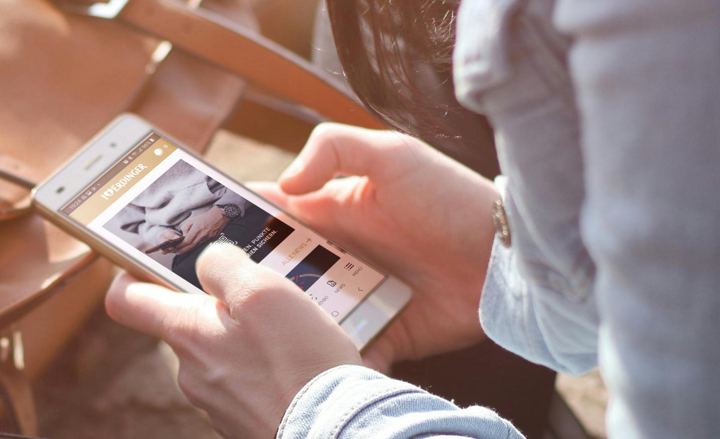 Eine Person mit einem Smartphone auf dem die geöffnete ERDINGER Fan App zu sehen ist in den Händen.