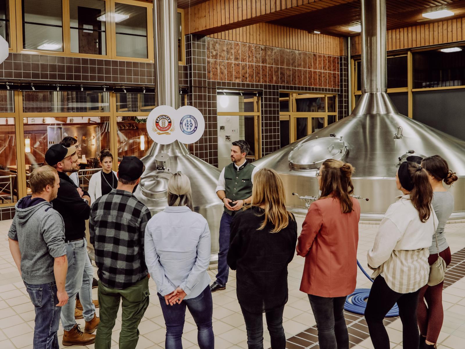 A brewery guide explains something to a group in the brewhouse.