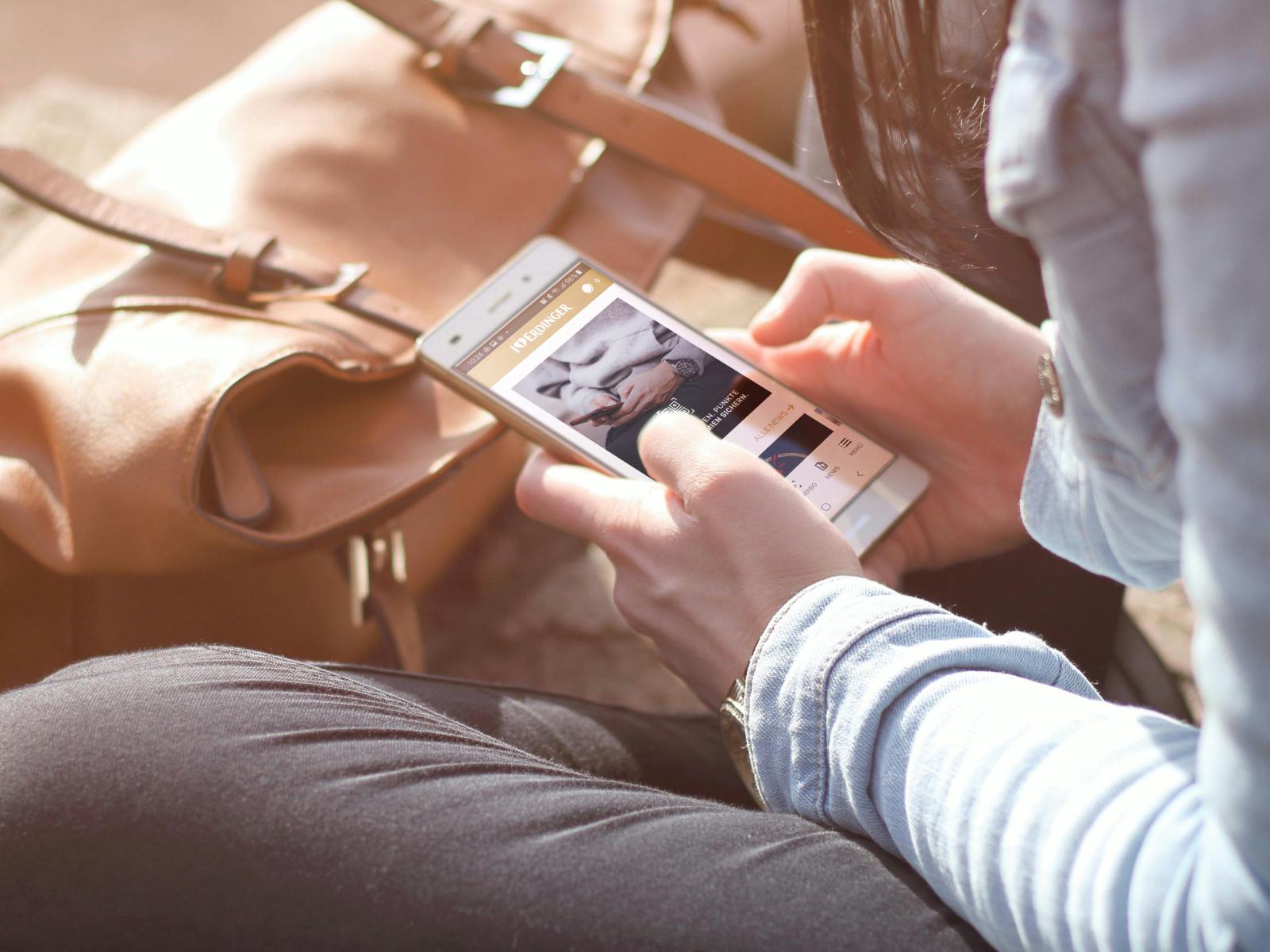 Eine Person mit einem Smartphone auf dem die geöffnete ERDINGER Fan App zu sehen ist in den Händen.