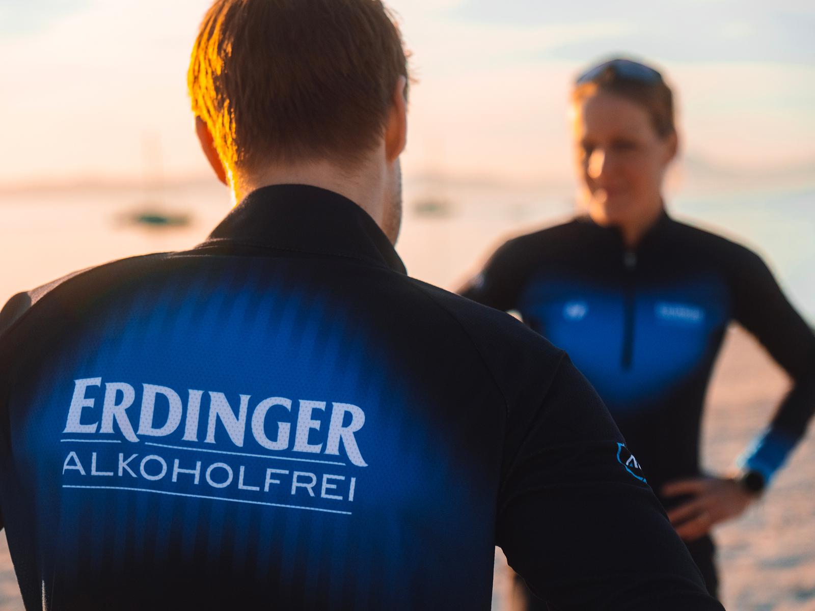 Zwei Personen mit ERDINGER Alkoholfrei Sportbekleidung prosten sich zu.