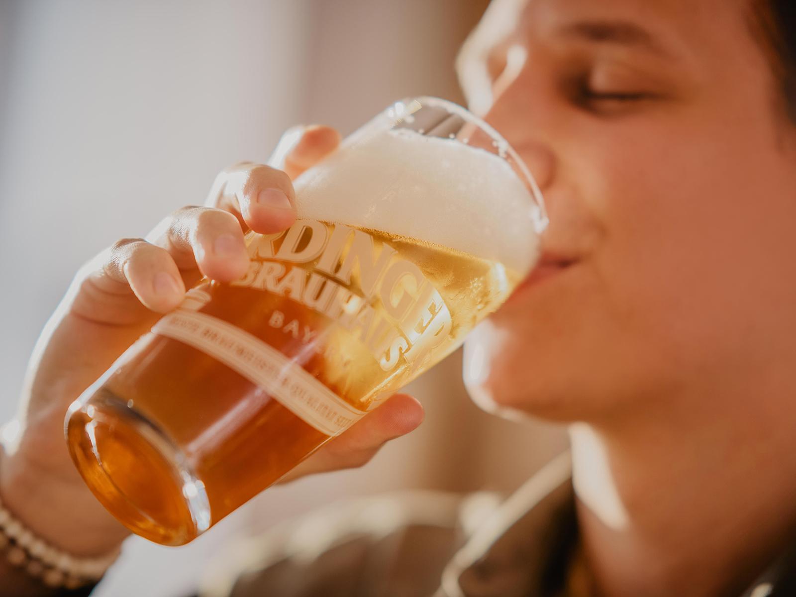 A close-up of a hand taking one of the many ERDINGER wheat beer glasses lined up on the shelf.