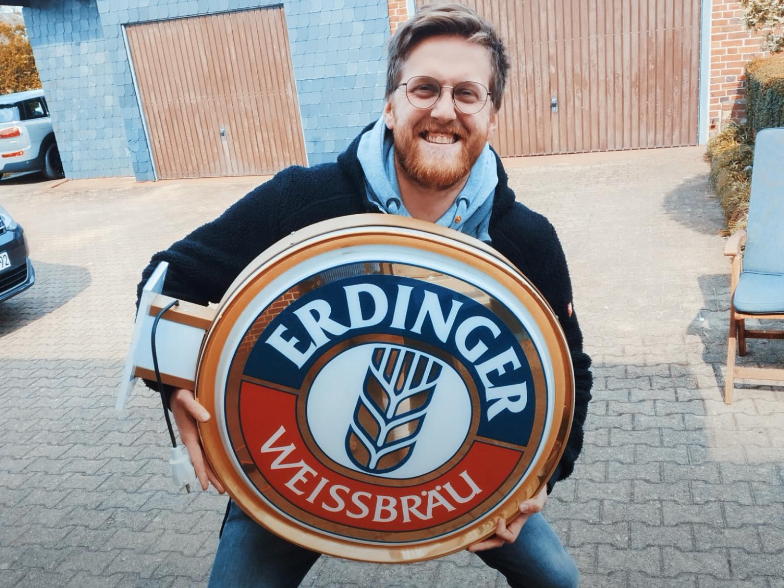 A man holds an old ERDINGER neon sign in his hands and smiles.