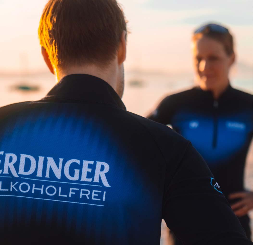 Zwei Personen mit ERDINGER Alkoholfrei Sportbekleidung prosten sich zu.