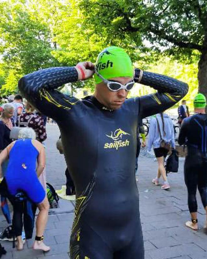 A man in a wetsuit and swim cap puts on swimming goggles.