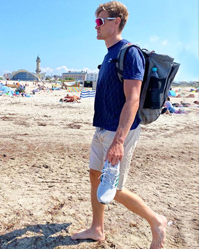 A man with a backpack is running along a beach.
