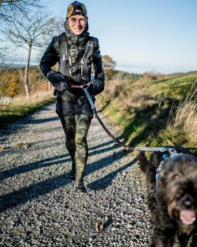 A smiling woman is walking with her dog in nature.