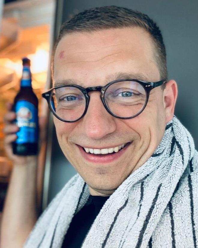 A man with a towel over his shoulder smiles while holding an ERDINGER Alcohol-Free.