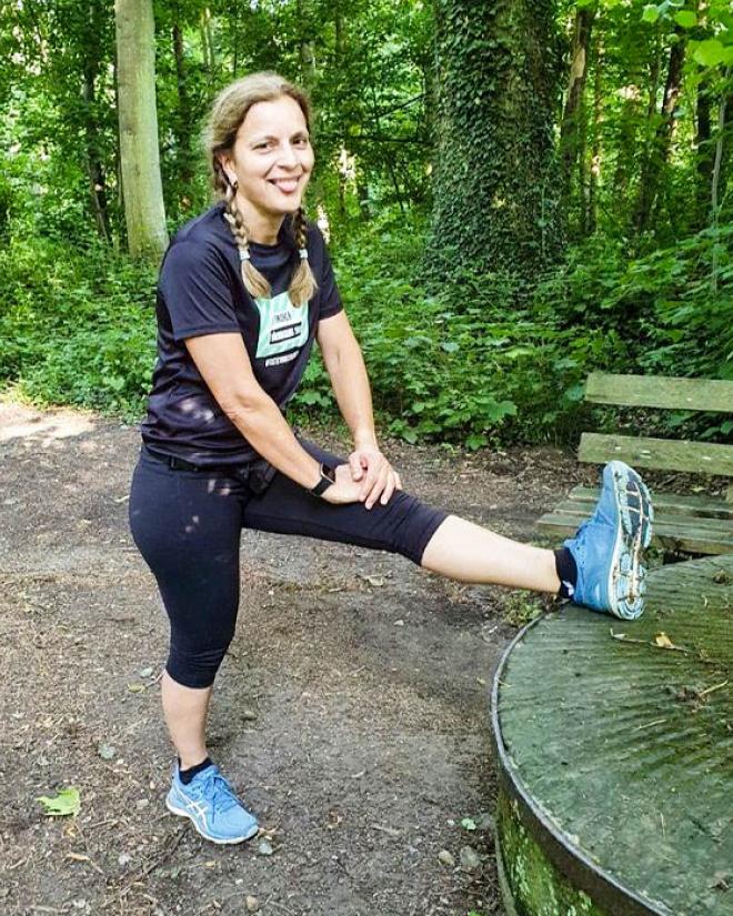 A woman is stretching before her run in nature, next to an old moss-covered millstone.
