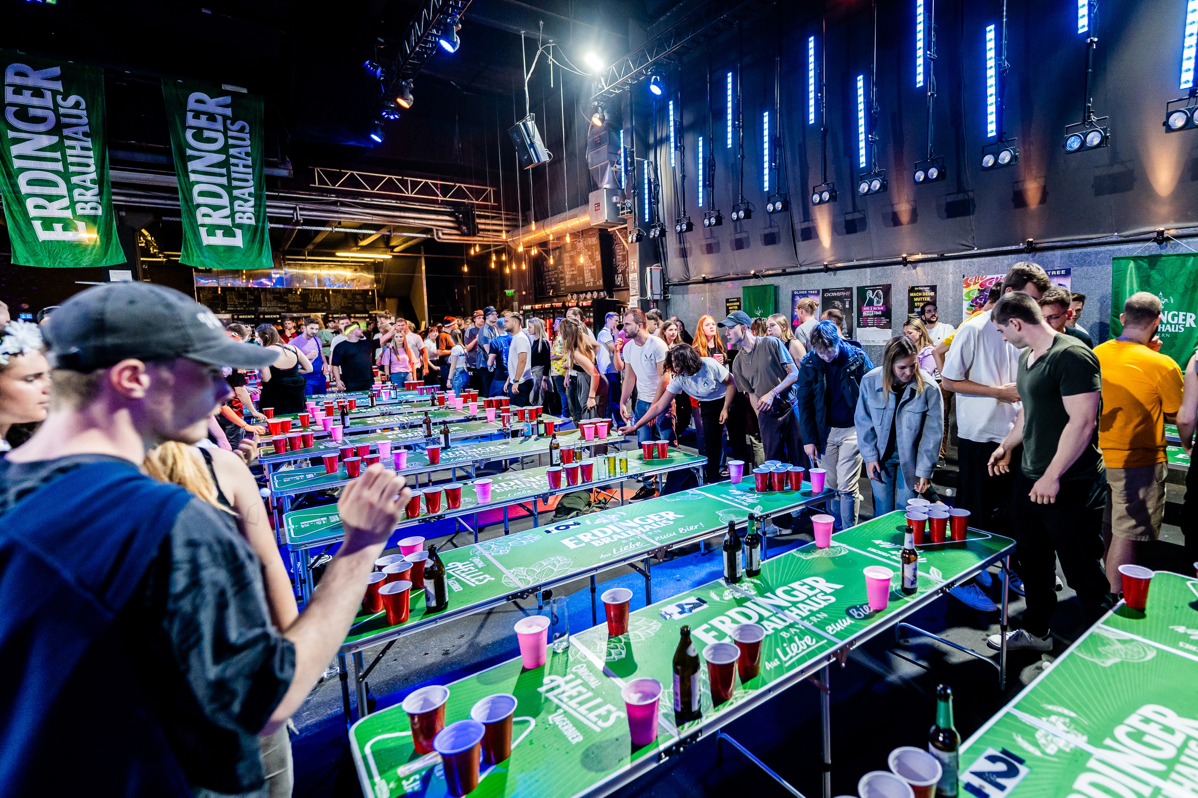 People are playing at several ERDINGER Brauhaus tables in a tournament of the BPong Bundesliga, with the BPBL logo in the corner.