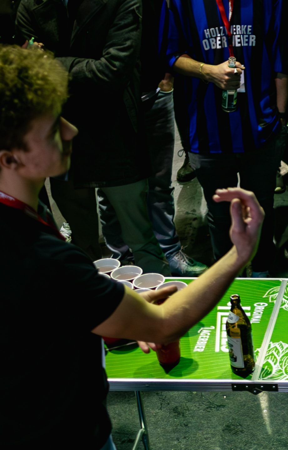 A man is gesturing in front of an ERDINGER Brauhaus beer pong table at a tournament.