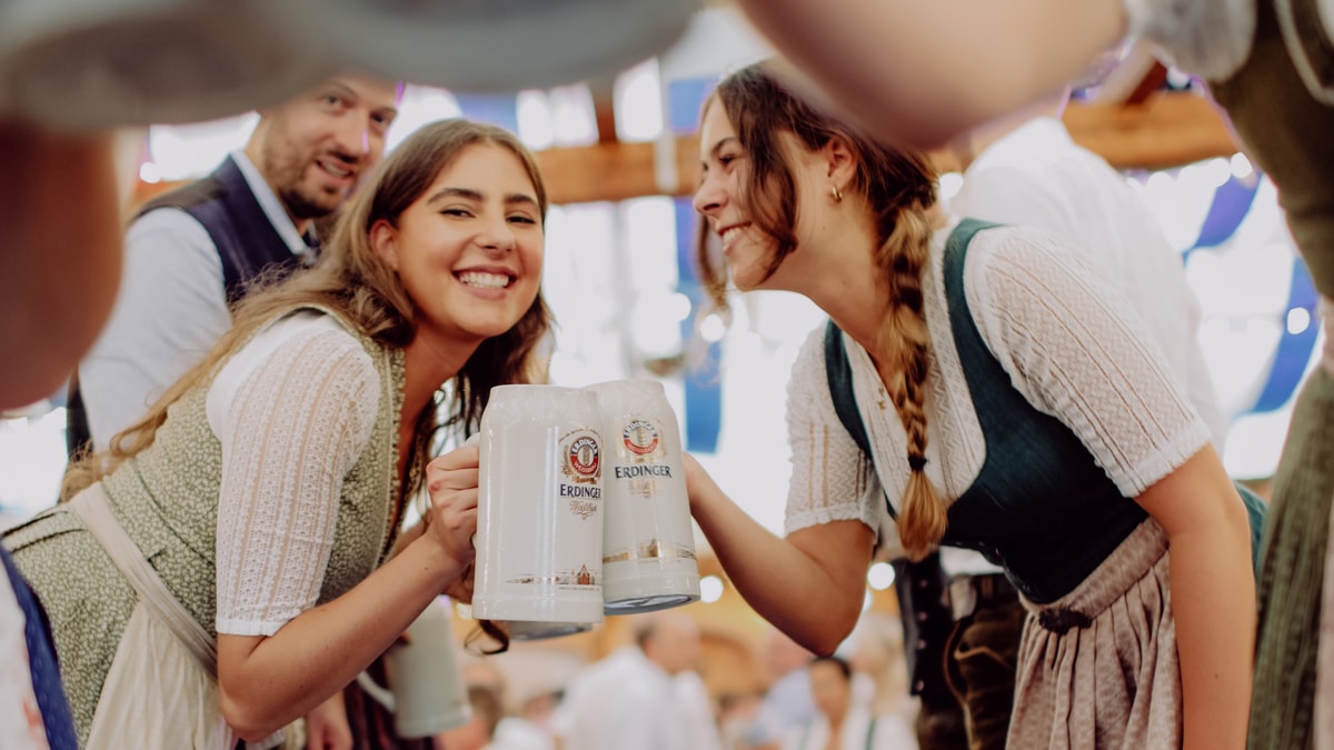 Two ERDINGER employees in traditional Bavarian attire toast each other with large beer mugs in the beer tent at the brewery‘s autumn festival.