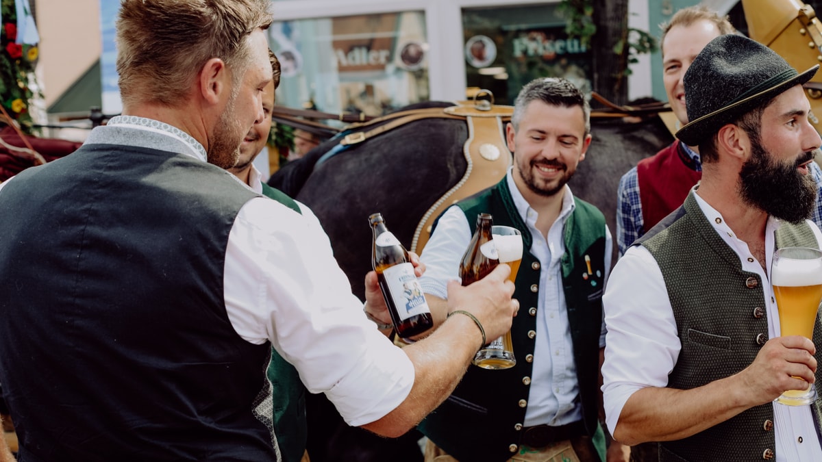 Several ERDINGER employees in traditional Bavarian attire toast each other during a parade at the brewery.