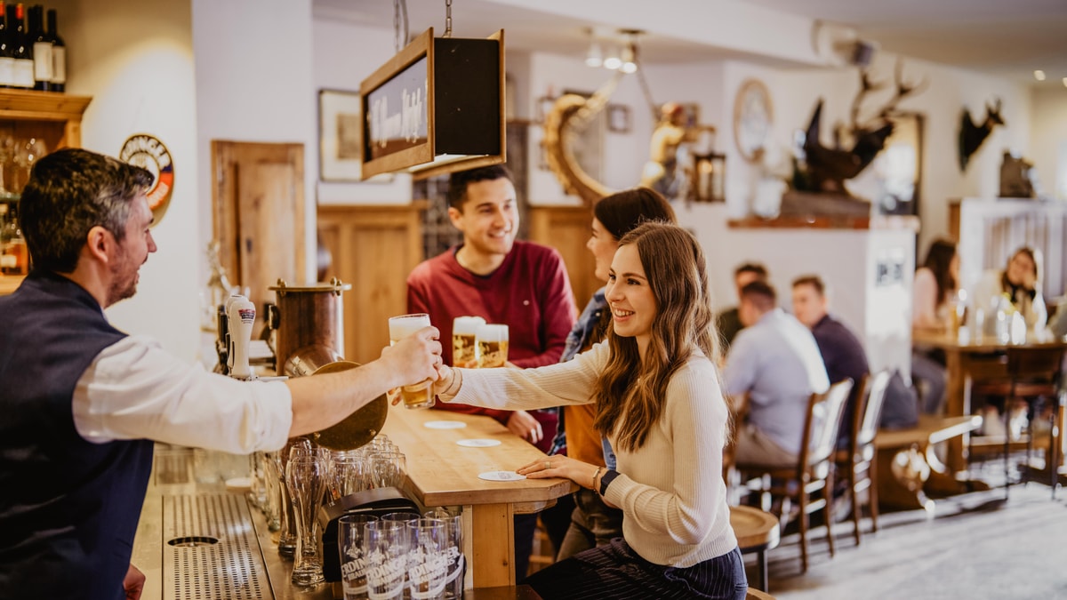 An ERDINGER employee hands a beer to a smiling woman over the bar counter in the brewery‘s visitor center.