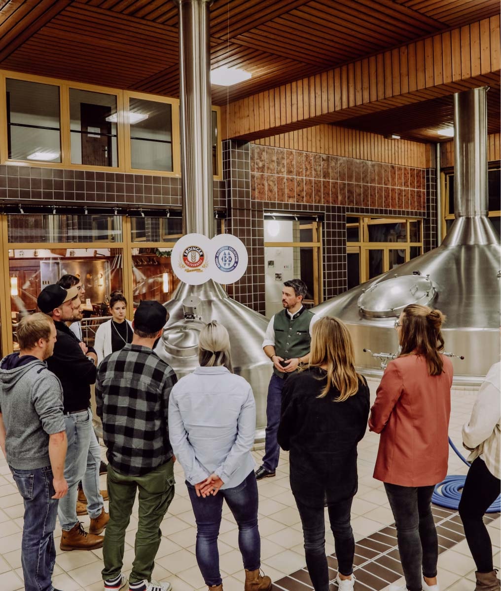 A brewery guide is explaining something to a group in the brewhouse.