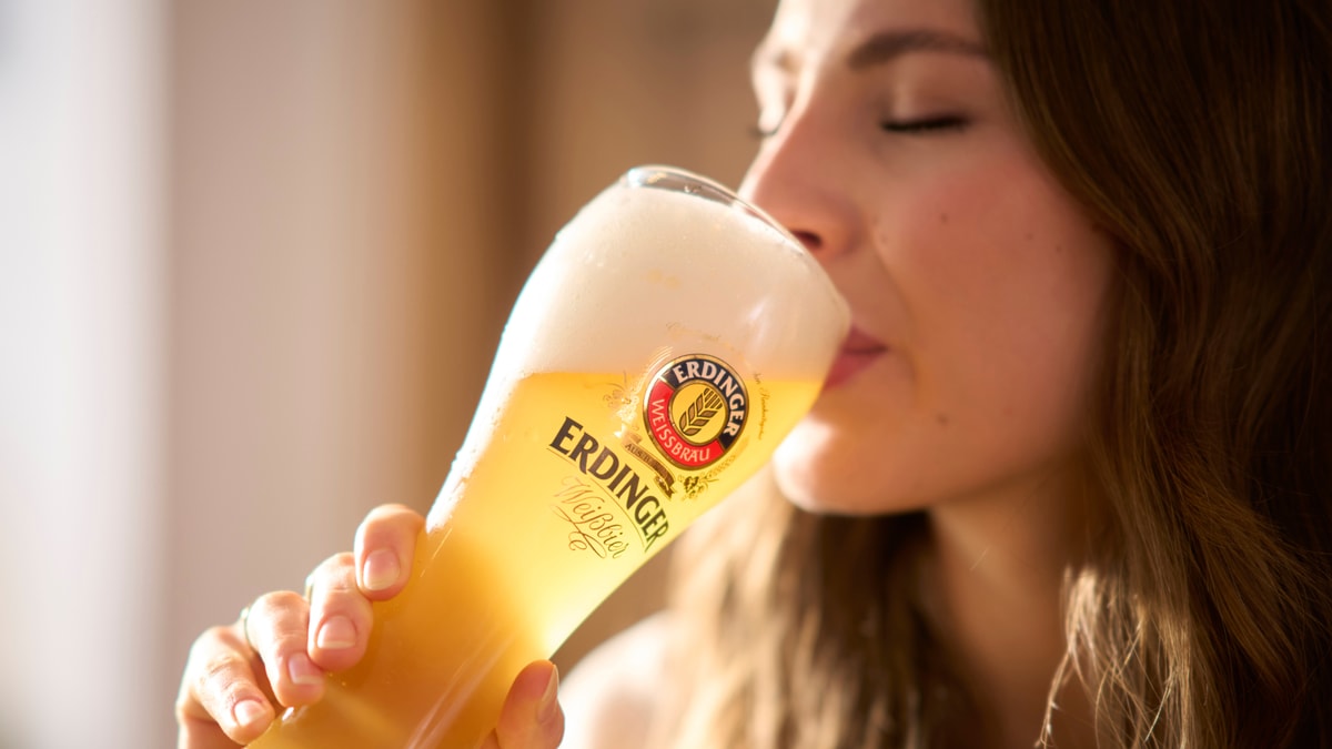 A woman takes a delightful sip of ERDINGER wheat beer from the glass.