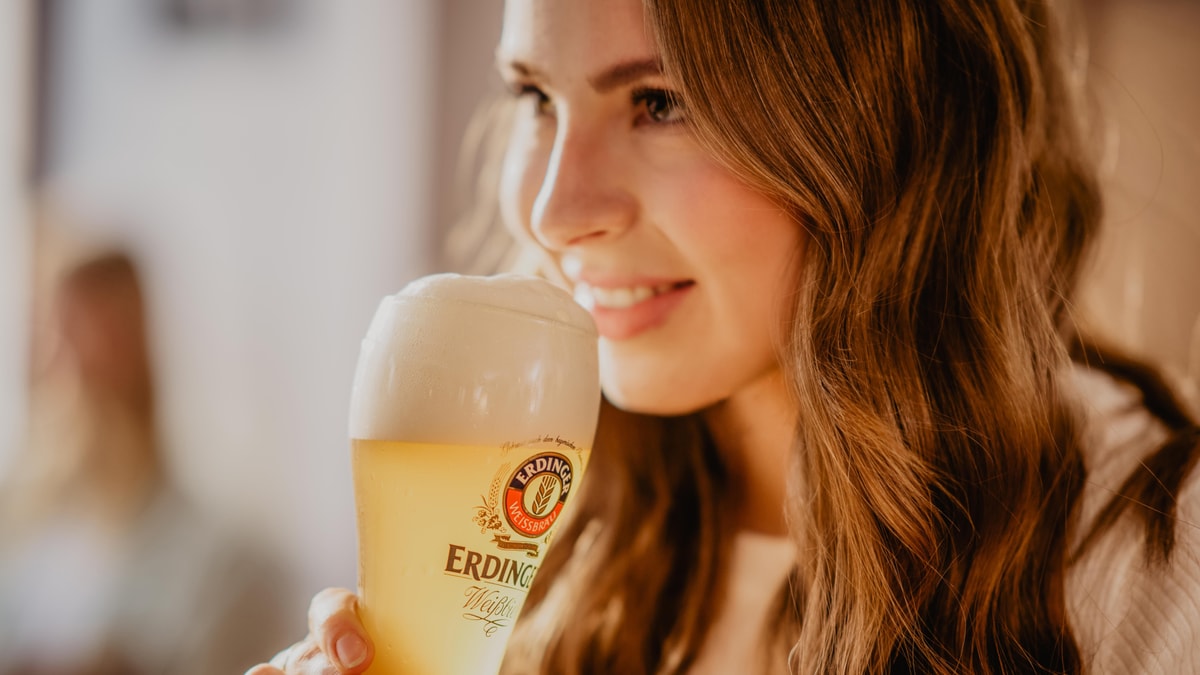 A woman smells an ERDINGER wheat beer in a glass.