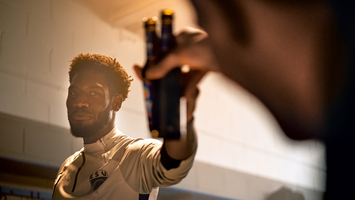Two men toast each other with ERDINGER Alkoholfrei in a locker room after training.