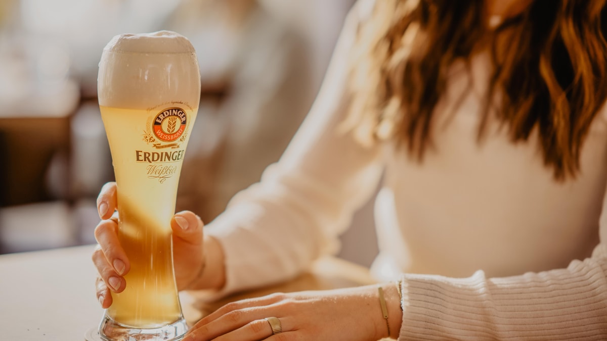 A woman reaches for a glass of ERDINGER wheat beer on a table.