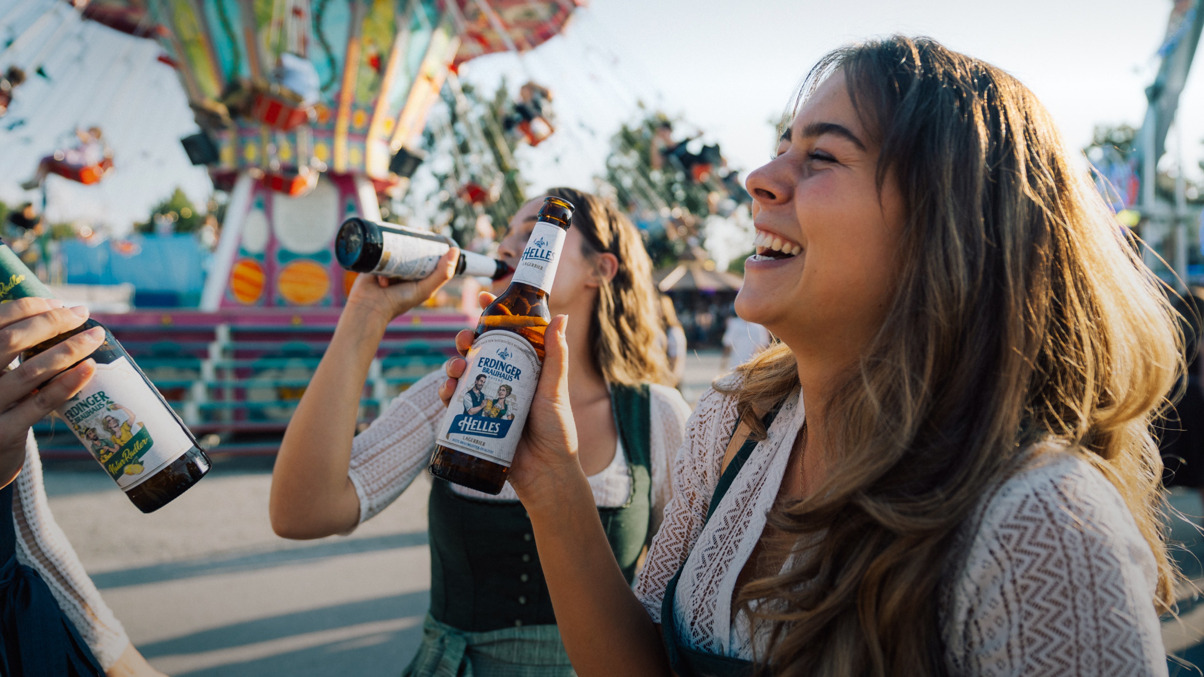 A woman is laughing and holding an ERDINGER Brauhaus Helles in her hand at a folk festival.