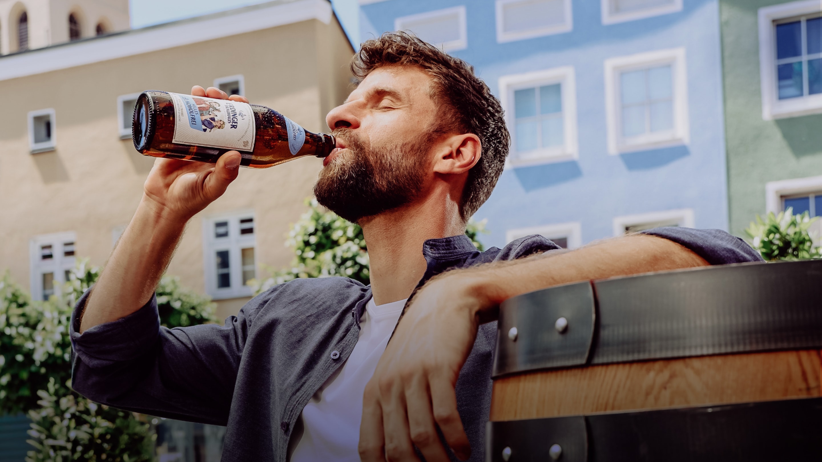 Thomas Müller lehnt an einem Holzfass im sommerlichen Erding und genießt ein ERDINGER Brauhaus Alkoholfrei.