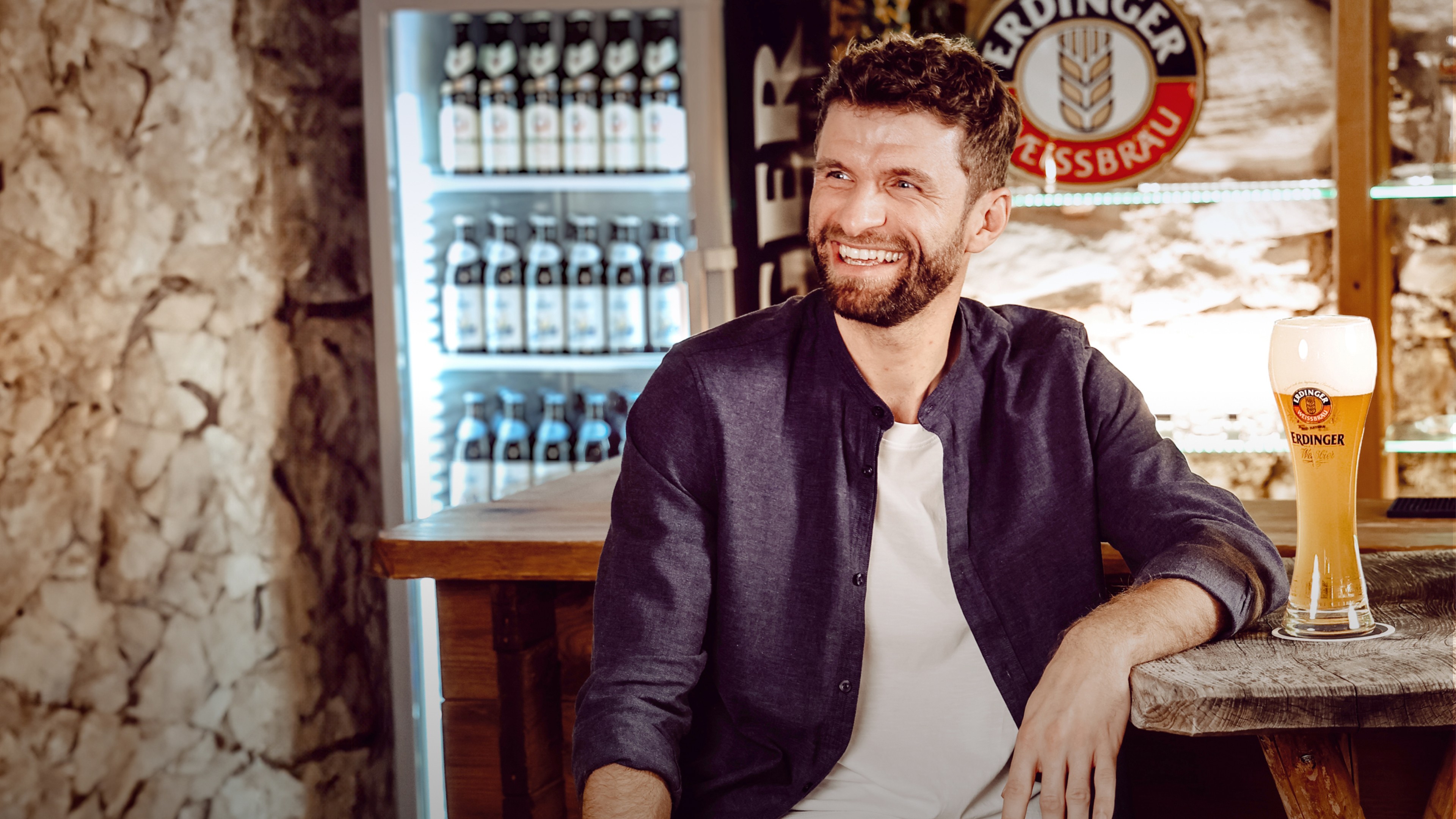 Thomas Müller smiles as he enjoys an ERDINGER Weißbier at the bar.