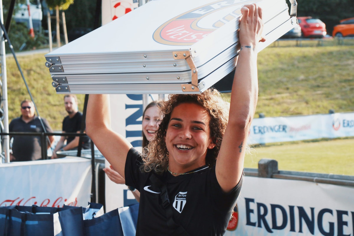 Eine Frau hält jubelnd den beim Fußballturnier gewonnen Bierpongtisch über den Kopf beim ERDINGER Meistercup.