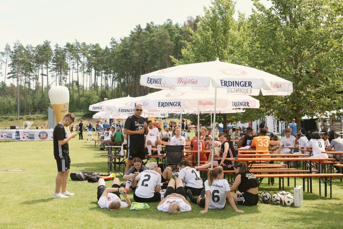 Spielerinnen ruhen sich bei einer Trinkpause im Schatten eines Schirms aus beim ERDINGER Meistercup.