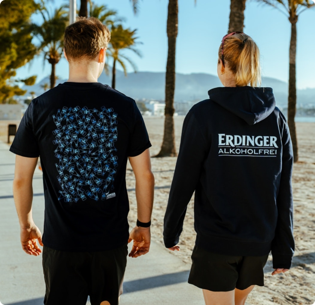 Zwei Personen mit ERDINGER Alkoholfrei Sportbekleidung prosten sich zu.