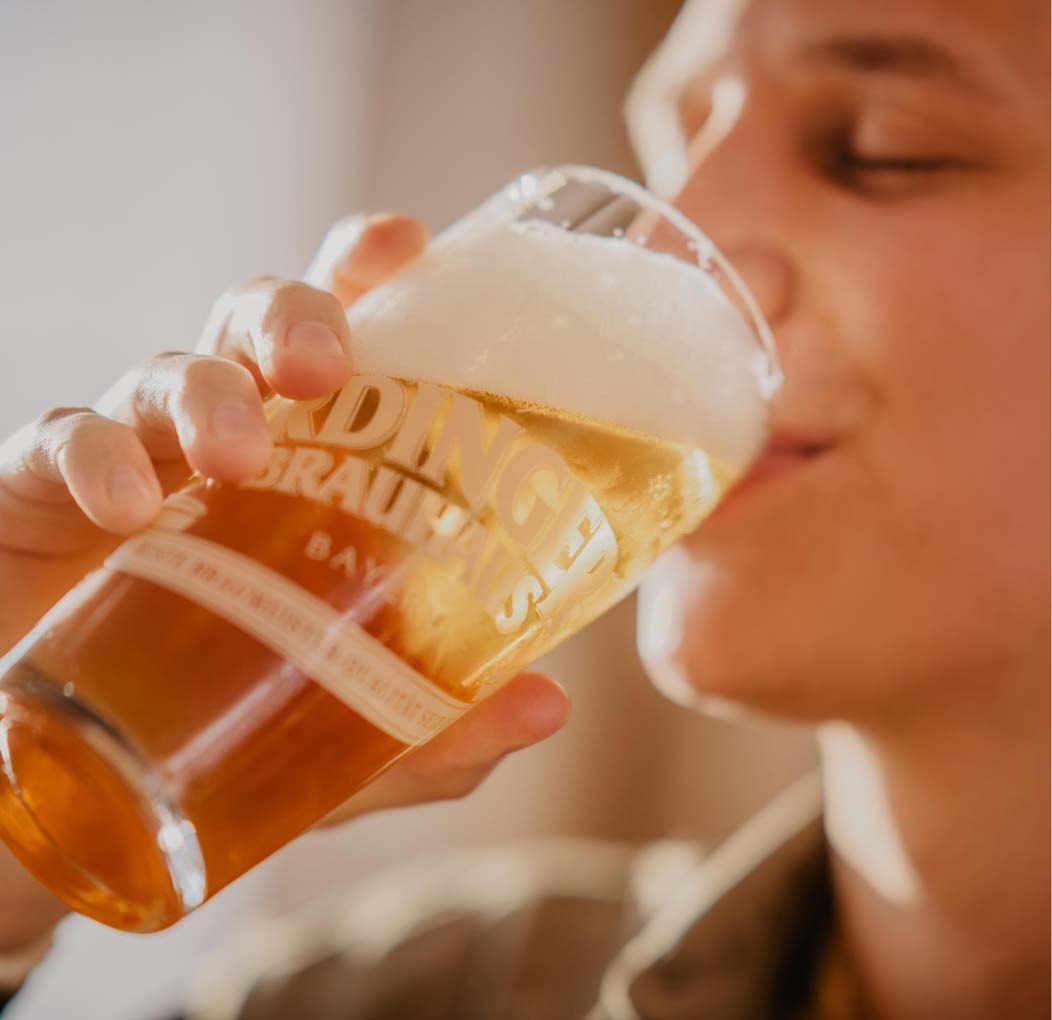 Ein Mann trinkt aus einem ERDINGER Brauhaus Willibecher.