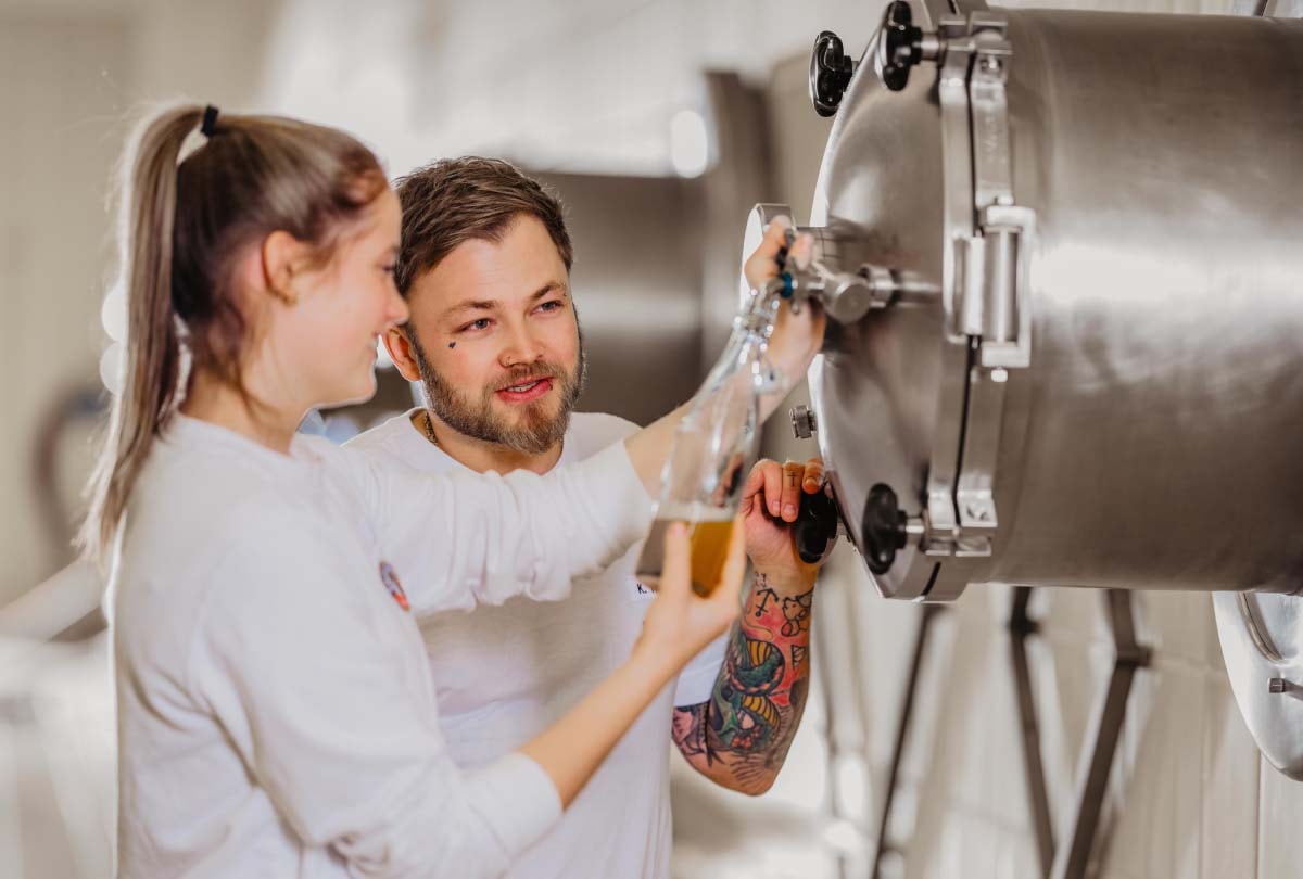 Two ERDINGER brewers are tasting beer in the fermentation cellar.