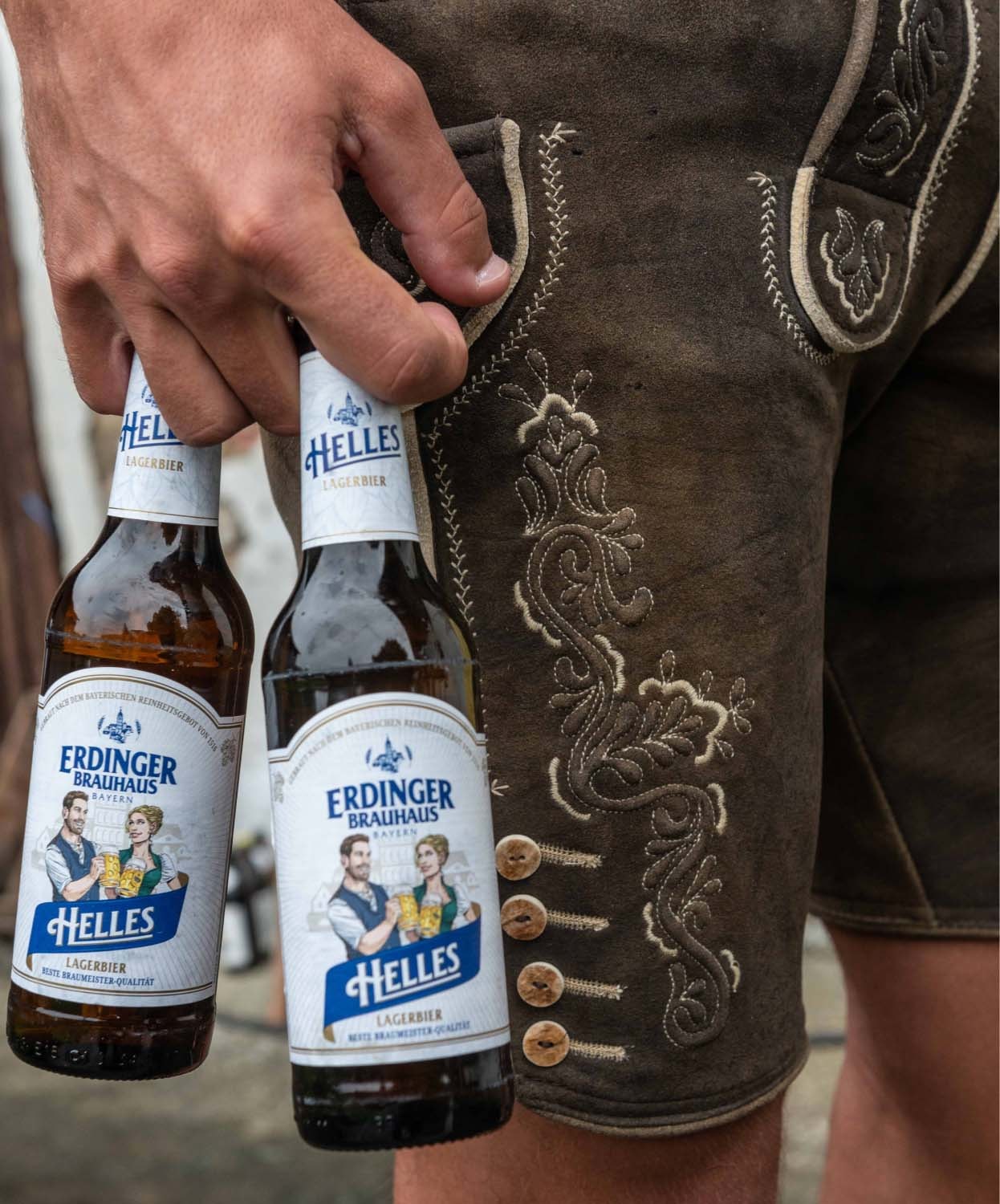 A man is holding two bottles of ERDINGER Brauhaus Helles in front of his leather trousers.