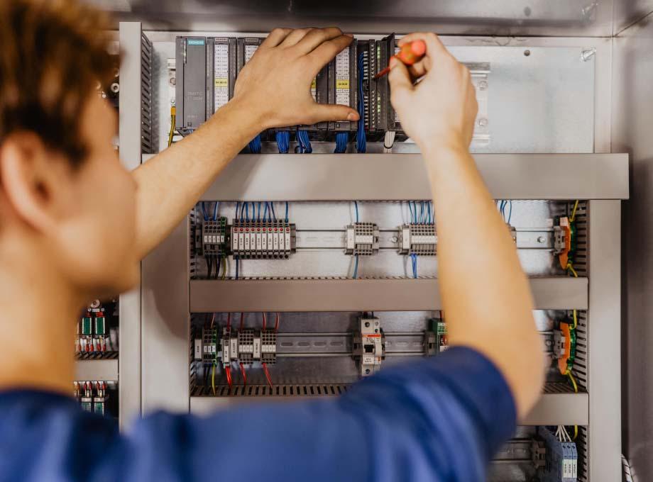 Blick über die Schulter eines ERDINGER Elektronikers der an einem Schaltkasten arbeitet.