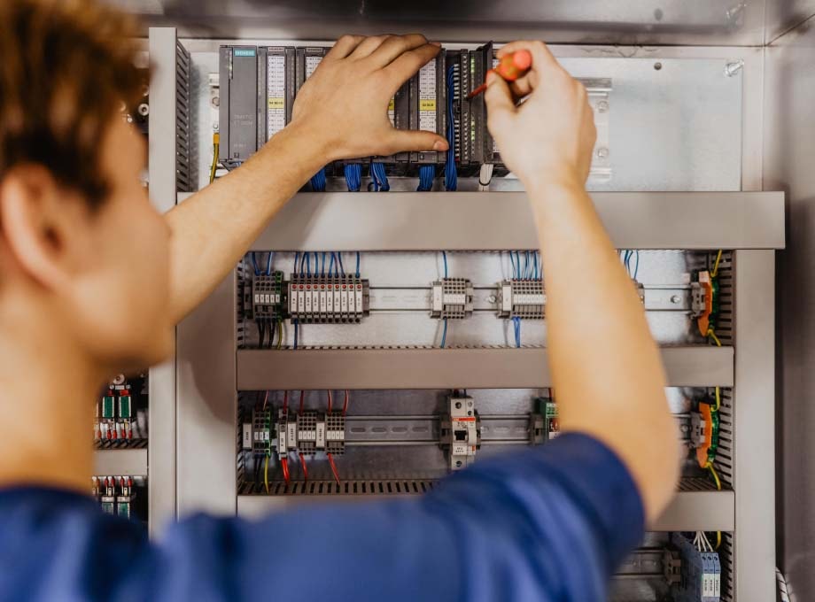 Blick über die Schulter eines ERDINGER Elektronikers der an einem Schaltkasten arbeitet.