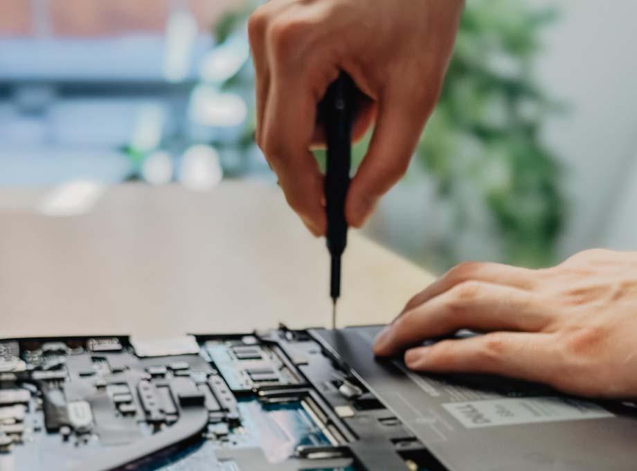 ERDINGER Fachinformatiker schraubt an offenem Laptop, Nahaufnahme der Hände.