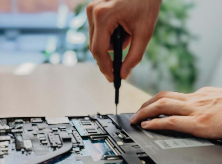 ERDINGER Fachinformatiker schraubt an offenem Laptop, Nahaufnahme der Hände.