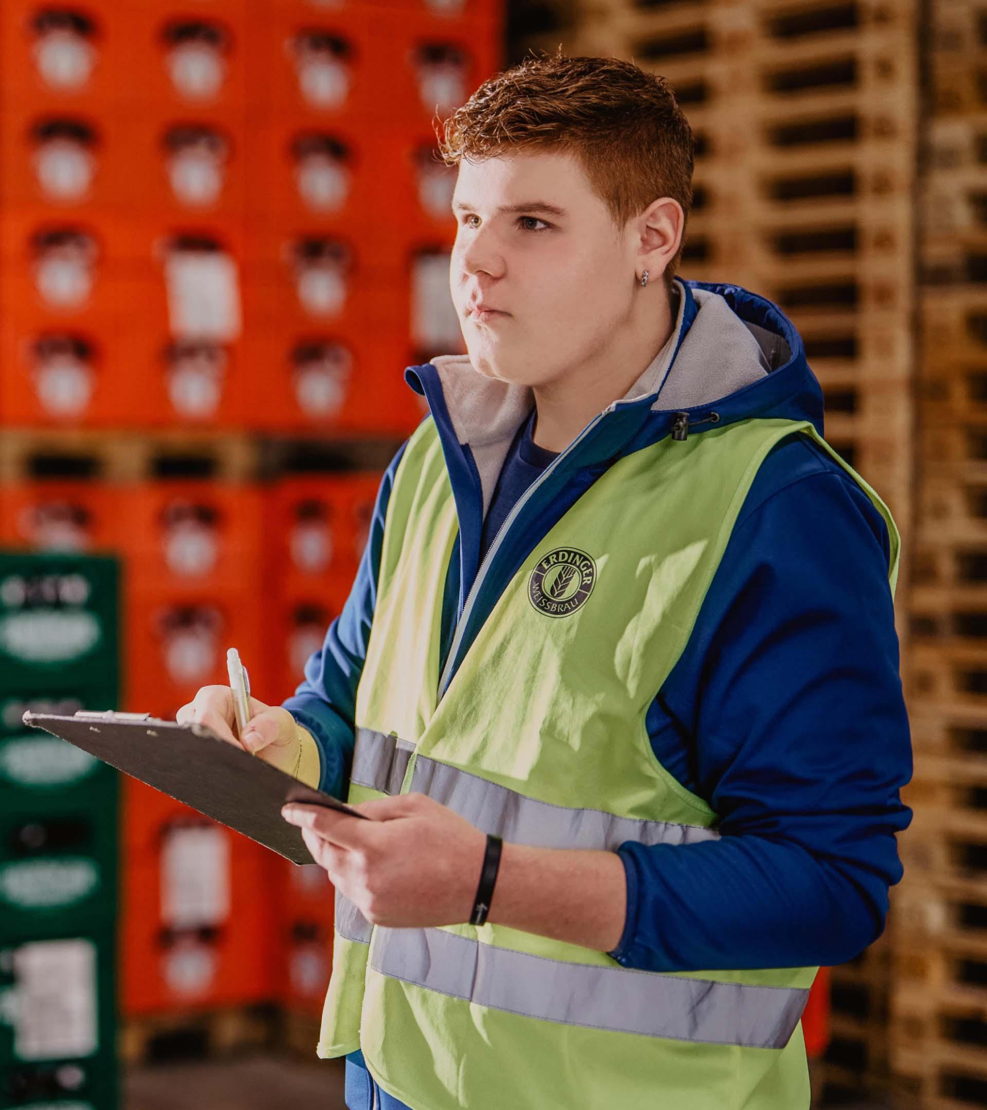 Ein ERDINGER Lagerlogistik Auszubildender arbeitet an einer Liste auf einem Klemmbrett.