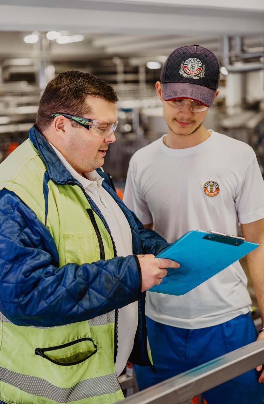 ERDINGER Lebensmitteltechniker zeigt einem Auszubildenden etwas auf einer Liste.