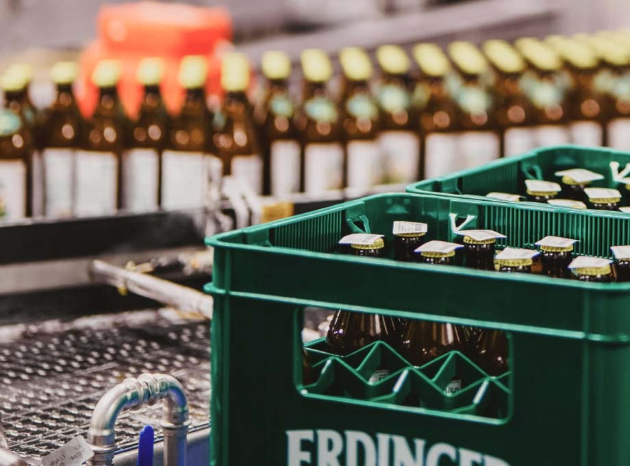 Eine Kiste ERDINGER Brauhaus Naturradler und einzelne Flaschen auf dem Band nach der Abfüllung.