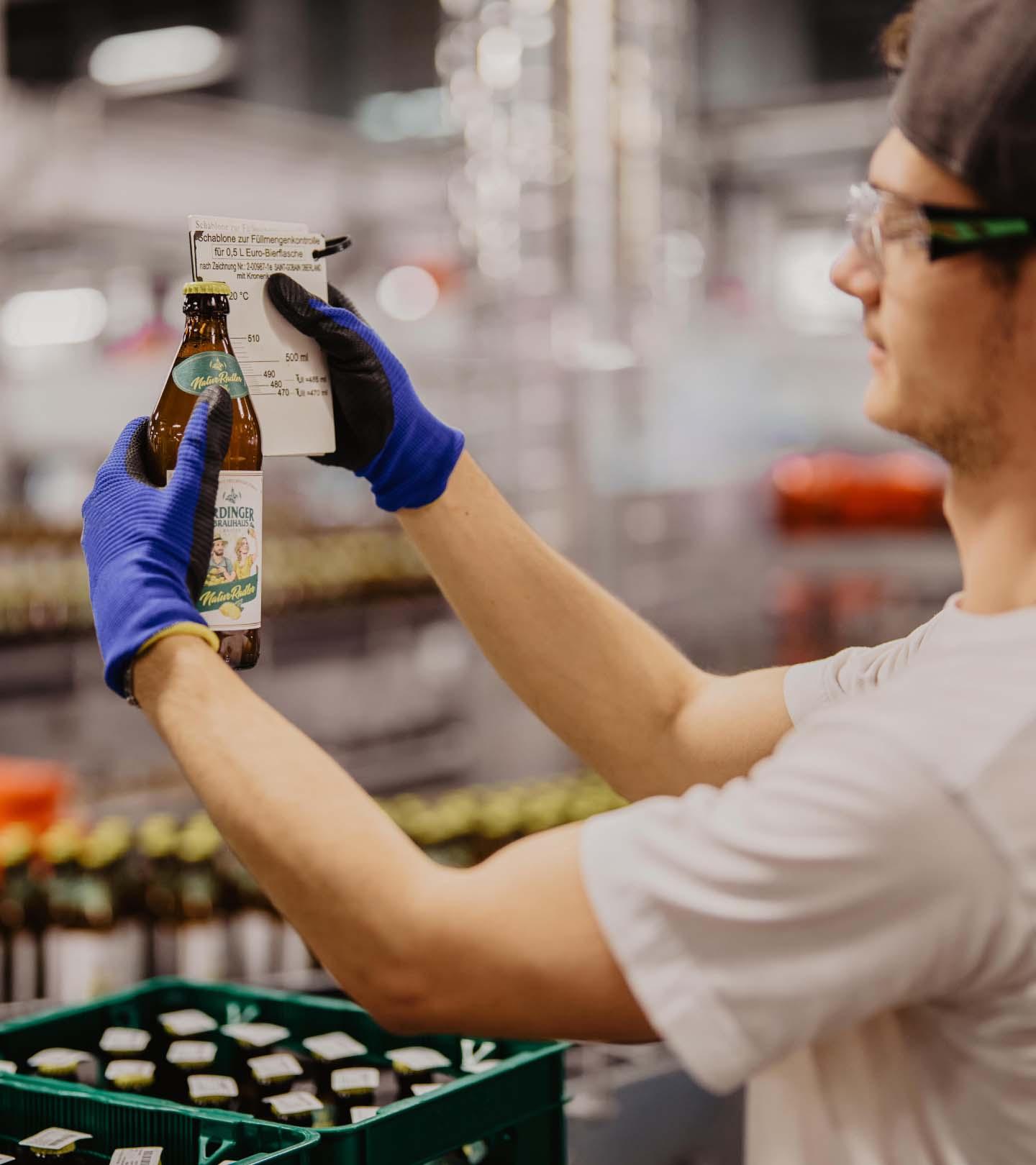 ERDINGER Lebensmitteltechniker prüft Füllmenge beim ERDINGER Brauhaus Naturradler mit einer Schablone.