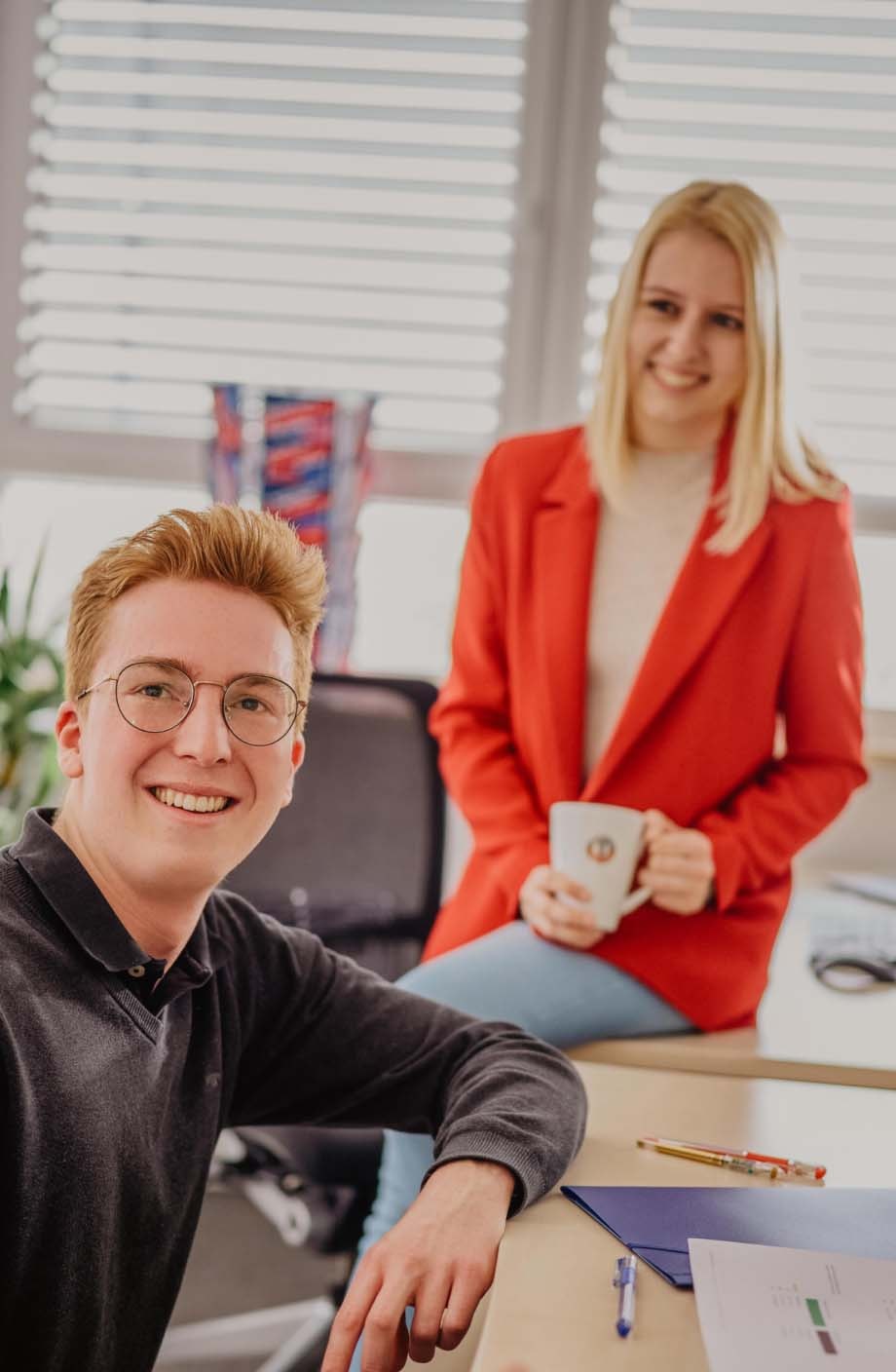 Zwei ERDINGER Industriekaufleute sitzen im Büro und lächeln.