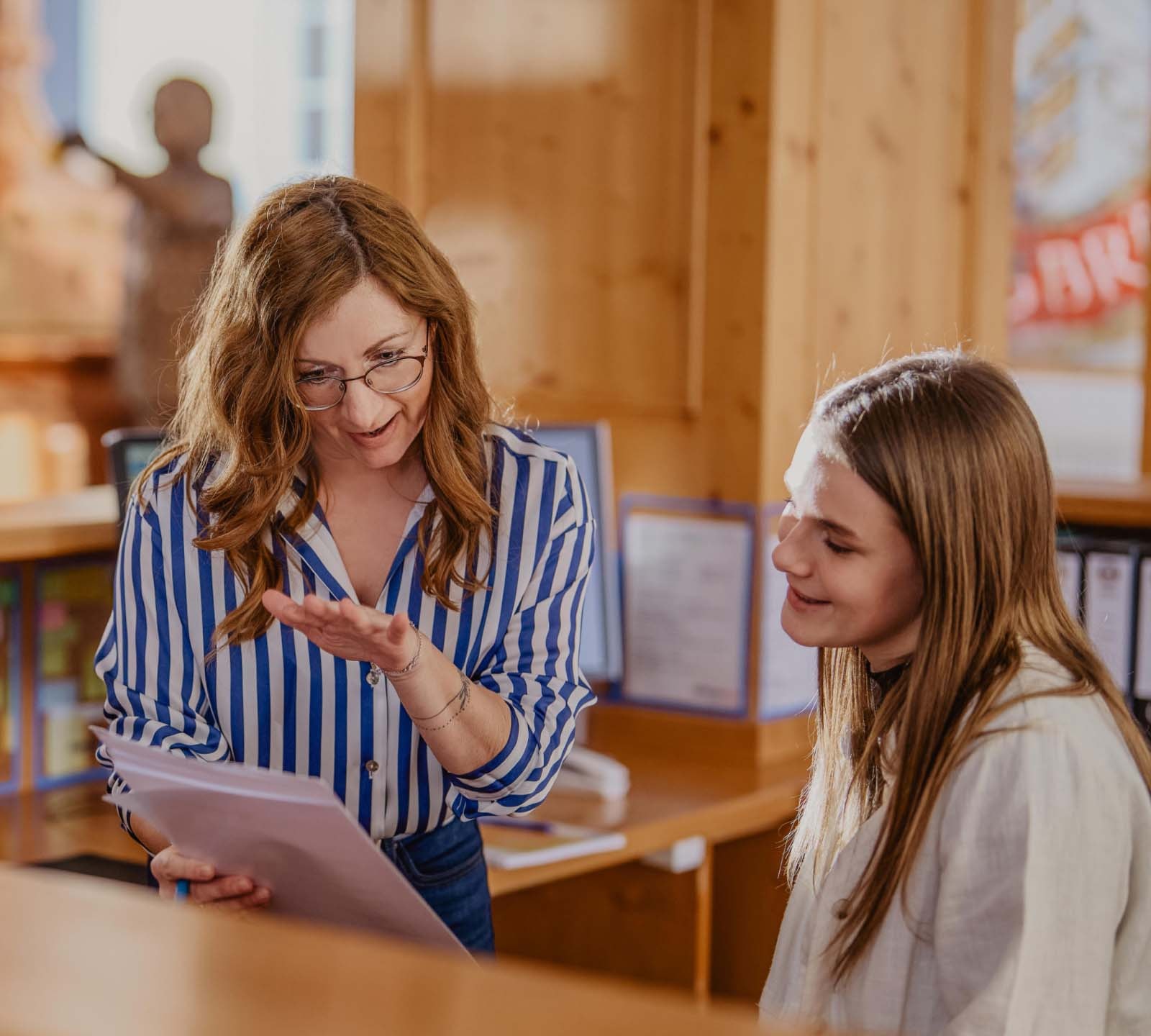 Zwei ERDINGER Industriekauffrauen sprechen über ein Dokument am Empfang.